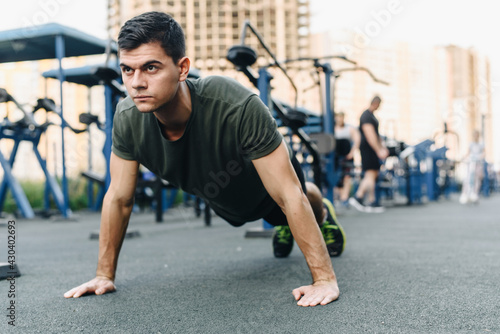 A young man does push-ups on the street on a specialized sports ground with trainers. Build muscles in the fresh air. Sport and healthy lifestyle concept