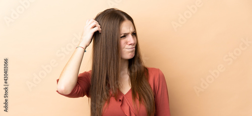 Young caucasian woman isolated on beige background having doubts while scratching head