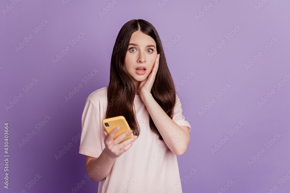 Photo of excited cute young woman hold cell phone touch face Photo of excited cute young woman hold cell phone touch face