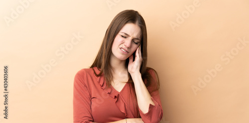 Young caucasian woman isolated on beige background with headache