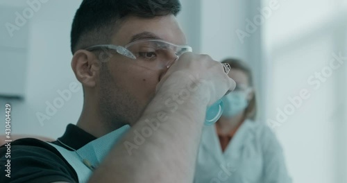 Close-up an Arabian patient who is taking a disposable glass of water and gargling his mouth while a female assistant is sitting next to him.