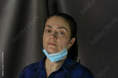 Portrait of a pretty white woman with a medical mask incorrectly dressed, the mask is lowered on the chin, no protection, dark gray background photo