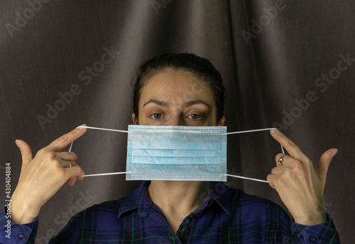 Portrait of a pretty white woman with a protective medical mask in her hands, taking care of her health, dark gray background photo