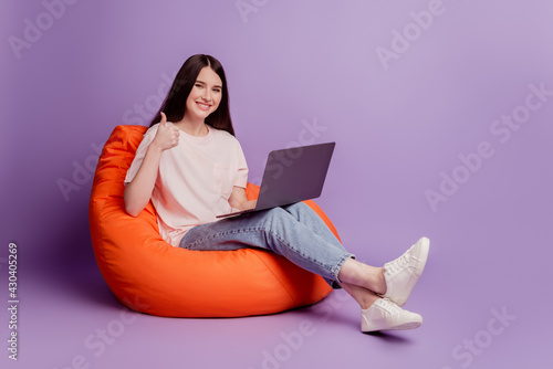 Photo of girl with laptop sit bean bag raise thumb up on purple background