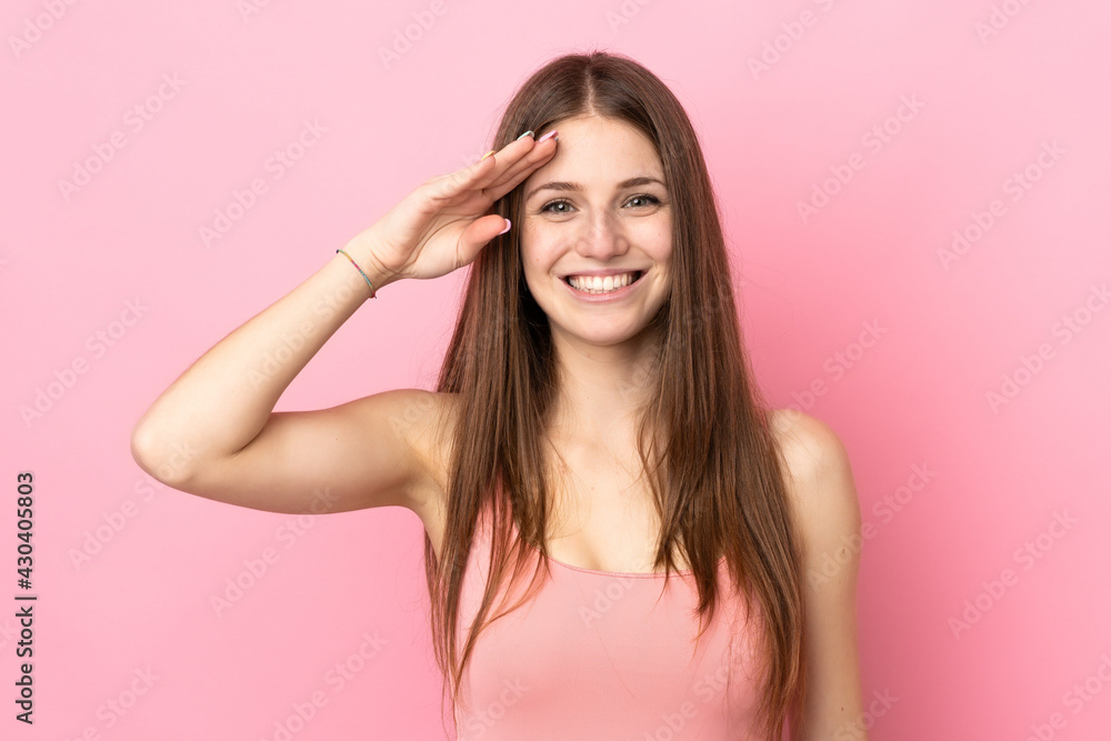Young caucasian woman isolated on pink background saluting with hand with happy expression