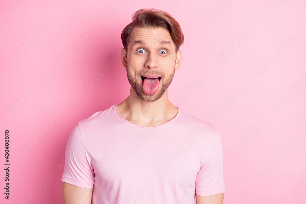 Photo of shocked childish young guy wear casual clothes showing tongue out isolated pink color background Photo of shocked childish young guy wear casual clothes showing tongue out isolated pink color background