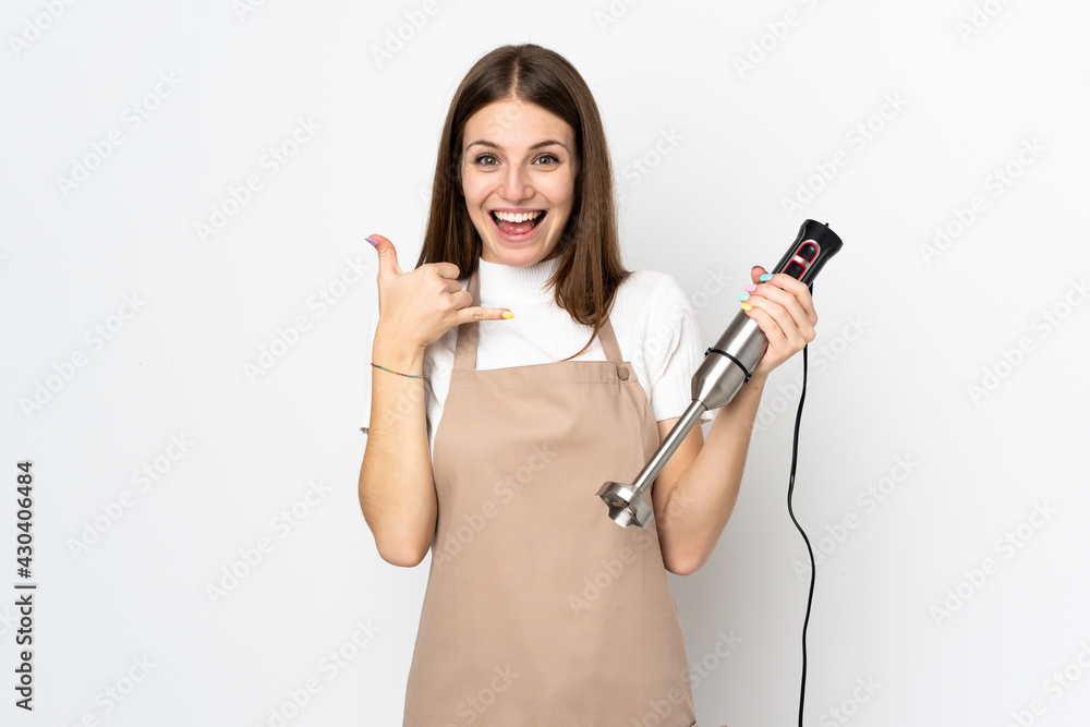 Young woman using hand blender isolated on white background making phone gesture Young woman using hand blender isolated on white background making phone gesture