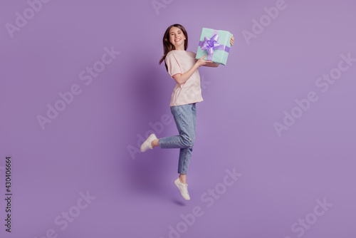 Portrait of adorable crazy girl jump carry persent giftbox posing on purple wall