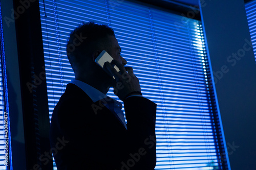 Uomo bianco biondo con tatuaggi vestito in giacca e camicia fa una chiamata dal cellulare in piedi  nel suo ufficio  photo