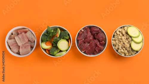 Fotografie Feeding bowls with natural pet food on orange background, flat lay