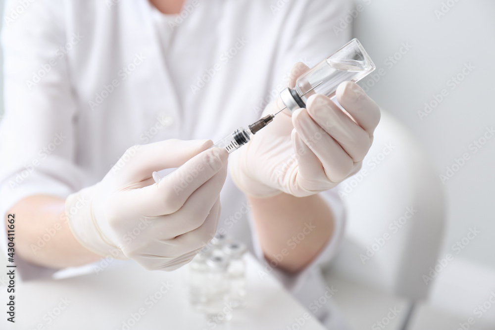 Doctor filling syringe with medication from vial on blurred background, closeup Doctor filling syringe with medication from vial on blurred background, closeup
