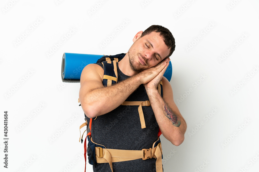 Brazilian mountaineer man with a big backpack over isolated white background making sleep gesture in dorable expression Brazilian mountaineer man with a big backpack over isolated white background making sleep gesture in dorable expression