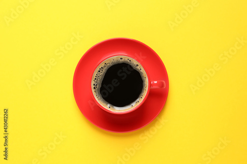 Aromatic coffee in red cup on yellow background, top view