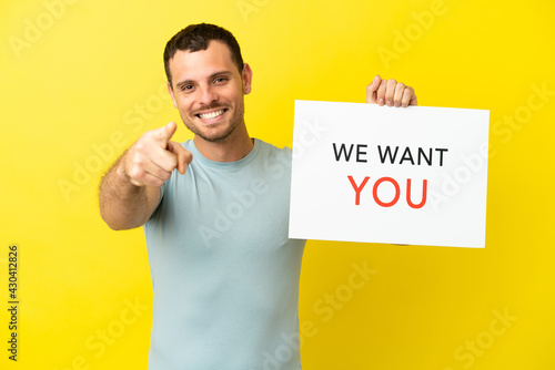 Bild auf Leinwand Brazilian man over isolated purple background holding We Want You board and poin