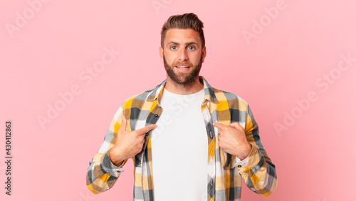 young handsome man feeling happy and pointing to self with an excited