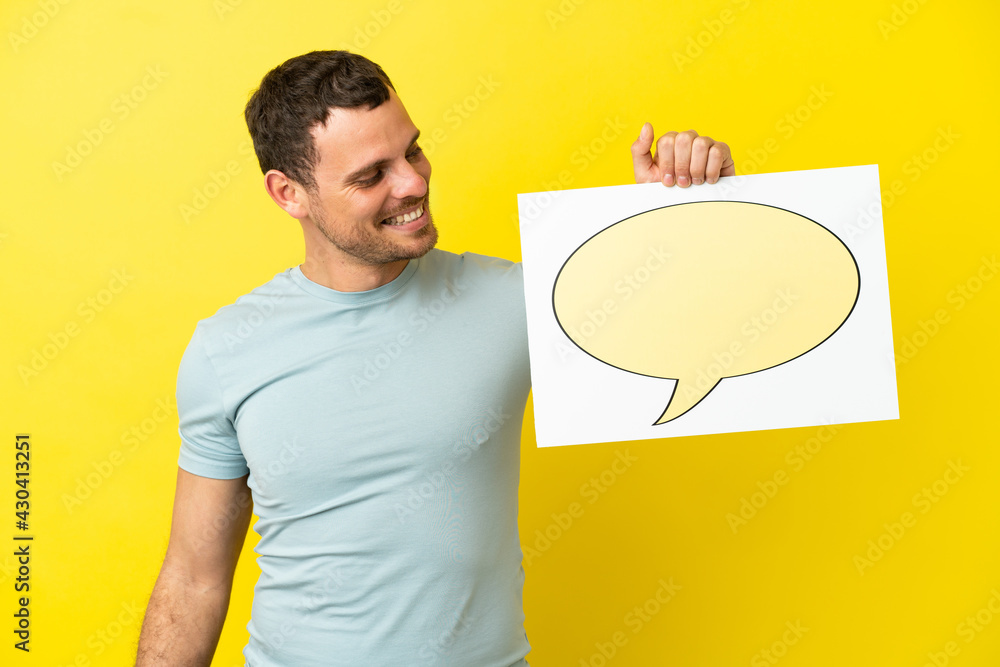Brazilian man over isolated purple background holding a placard with speech bubble icon Brazilian man over isolated purple background holding a placard with speech bubble icon