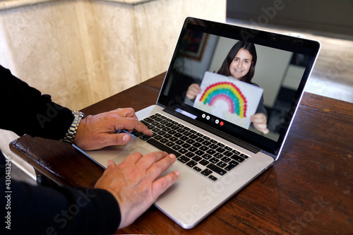 Video chiamata tra un adulto e una bambina che rtien in mano il disegno di un arcobaleno , attraverso un computer in contesto casalingo