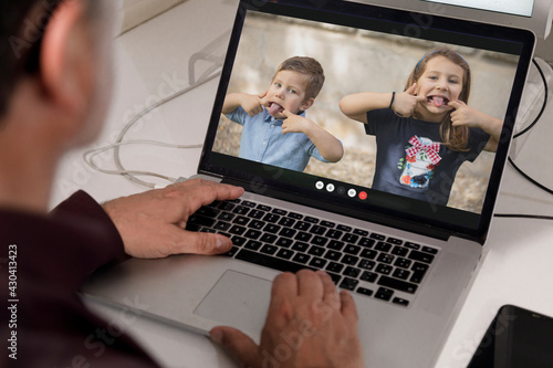 Video chiamata tra un adulto e due bambini che fanno le boccacce e giocano   attraverso  un portatile  in contesto  lavorativo photo