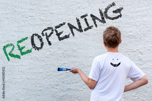 Ein Junge mit Pinsel steht vor einer weißen Wand mit dem schwarzen Text REOPENING, den er aufgemalt hat
