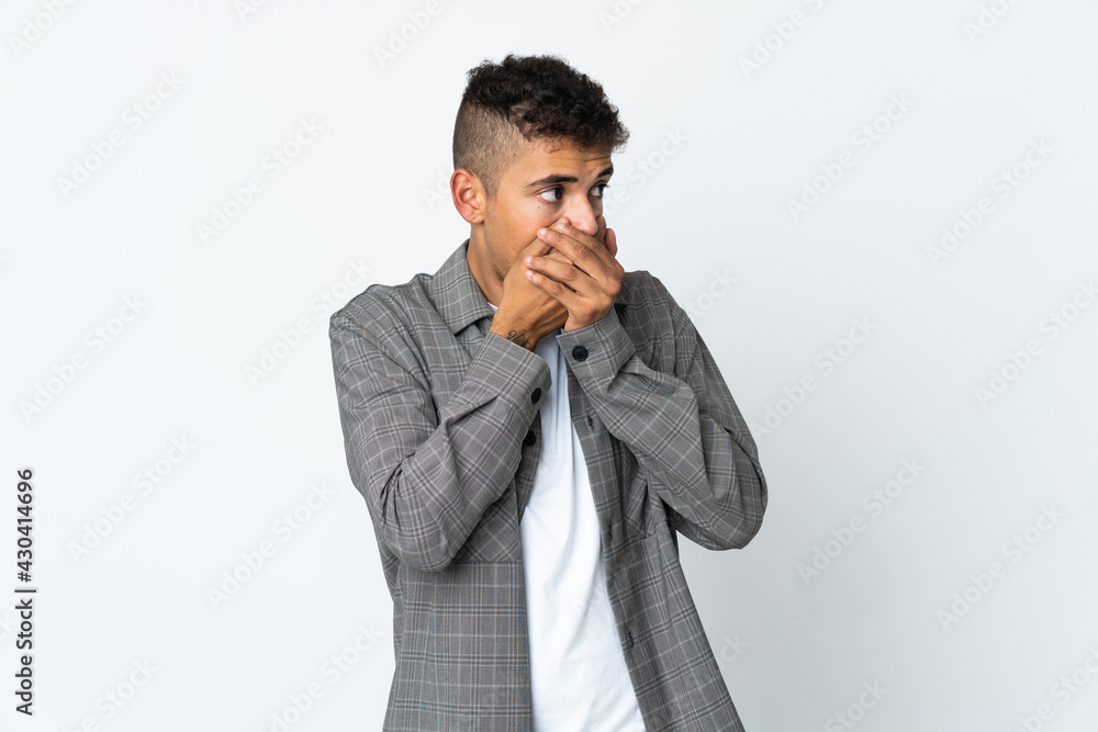Young brazilian man isolated on white background covering mouth and looking to the side Young brazilian man isolated on white background covering mouth and looking to the side