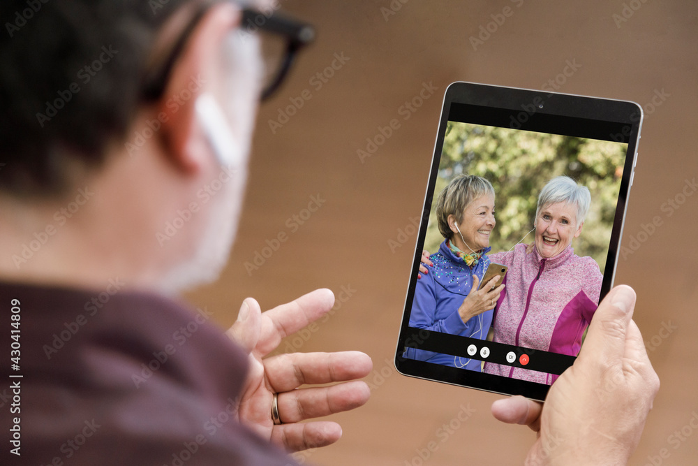Tablet tenuto in mano da un uomo , nel cui schermo compaiono due signore al parco in remoto in videoconferenza