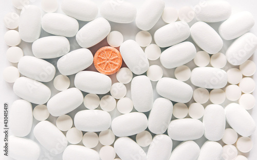 White pills on a white background. One bright orange round pill accent. Oblong and round pills close-up. Healthcare and medicine. © Olena Svechkova