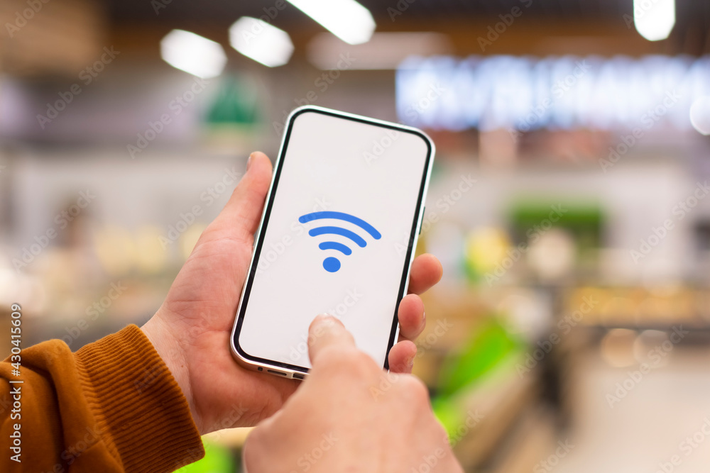 Free WiFi. Phone display with wi-fi icon against the backdrop of a restaurant. Man holds a smartphone in his hand close-up. Free WiFi. Phone display with wi-fi icon against the backdrop of a restaurant. Man holds a smartphone in his hand close-up.