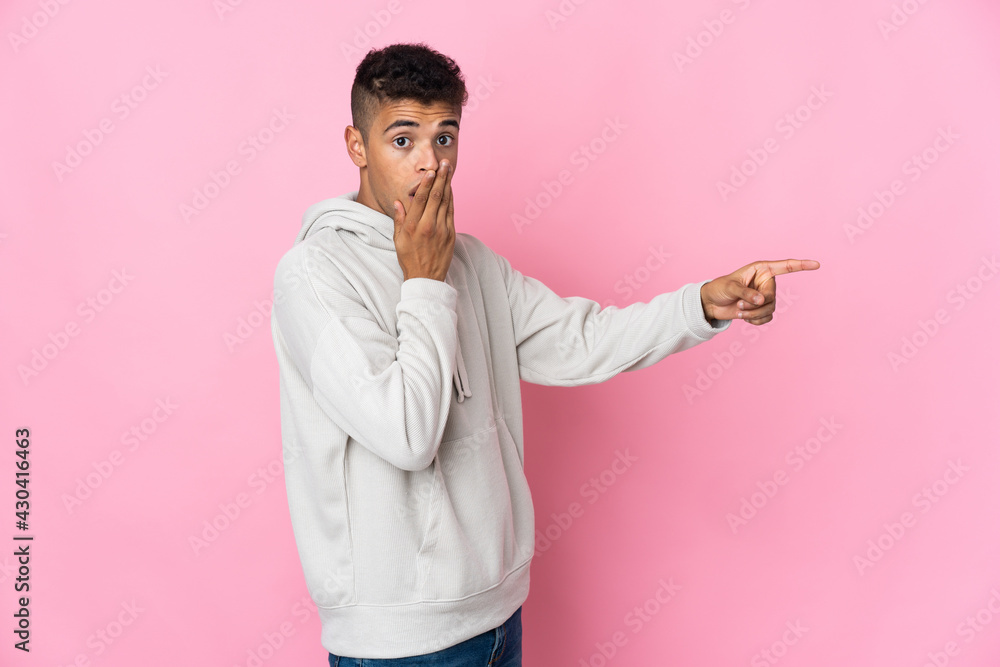 Young Brazilian man isolated on pink background with surprise expression while pointing side