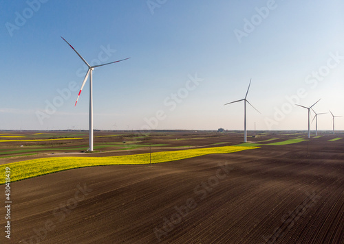 Aerial view of wind turbine. Rapeseed blooming. Windmills and yellow fields from above. Agricultural fields.Renewable Energy.