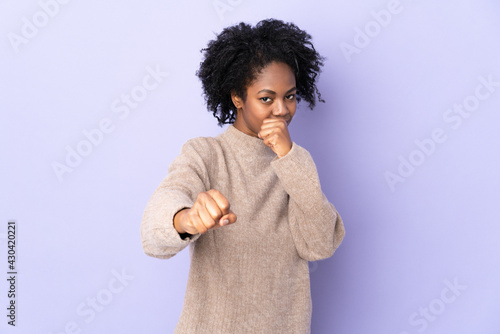 Young African American woman isolated on purple background with fighting gesture