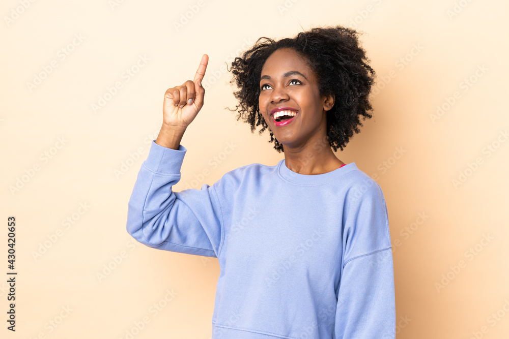 Young African American woman isolated on beige background pointing up and surprised Young African American woman isolated on beige background pointing up and surprised