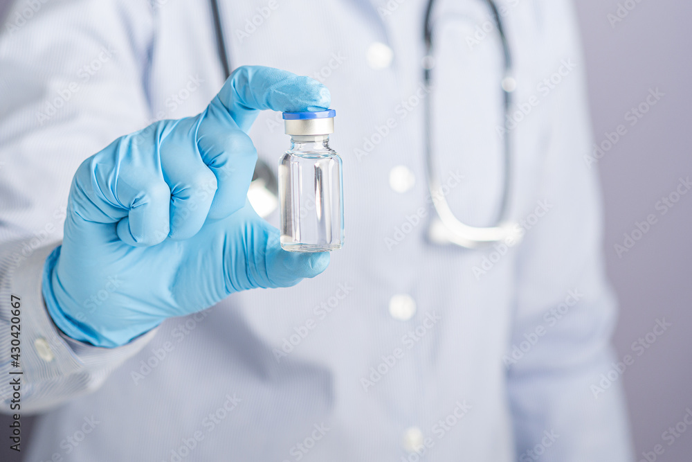 Doctor showing a vaccine bottle while standing with a gray background. Vaccine for immunization, and treatment from virus infection. Concept of medical and the fight against the virus Doctor showing a vaccine bottle while standing with a gray background. Vaccine for immunization, and treatment from virus infection. Concept of medical and the fight against the virus