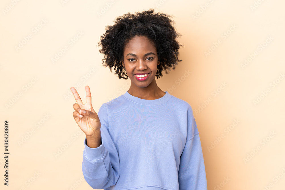 Young African American woman isolated on beige background smiling and showing victory sign Young African American woman isolated on beige background smiling and showing victory sign