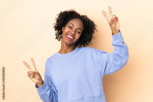 Young African American woman isolated on beige background showing victory sign with both hands