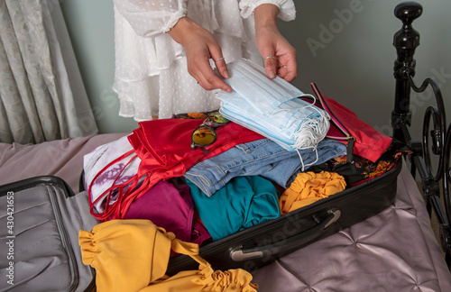 England, UK. 2021. Woman packing face masks and summer clothes into holiday suitcase in readiness of a covid outbreak.