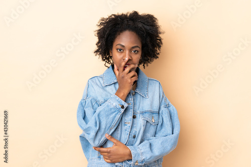 Young African American woman isolated on beige background surprised and shocked while looking right