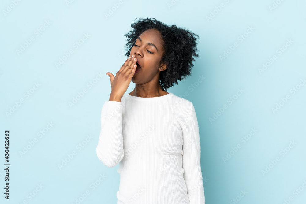 Young African American woman isolated on blue background yawning and covering wide open mouth with hand Young African American woman isolated on blue background yawning and covering wide open mouth with hand