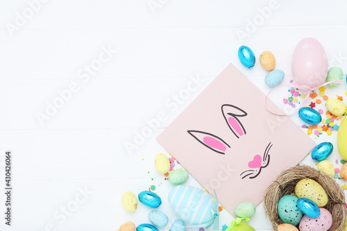 Easter concept. Rabbit on paper with colorful eggs and sprinkles on white wooden table