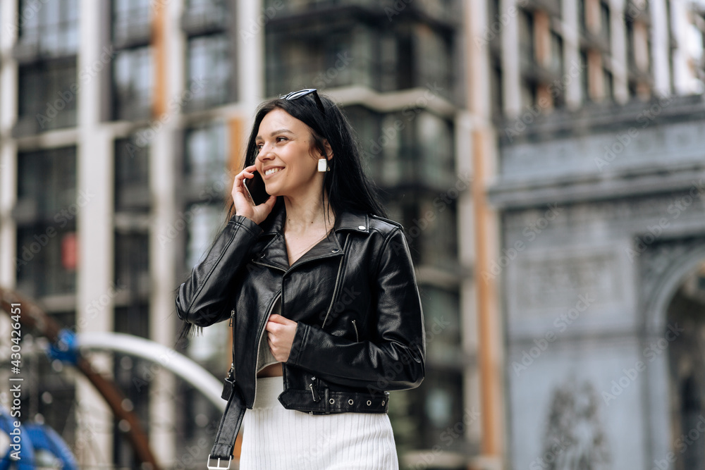 Happy young business woman talking on phone while walking on the street
