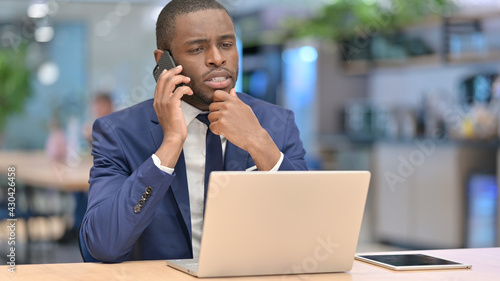 African Businessman with Laptop Talking on Phone in Office 