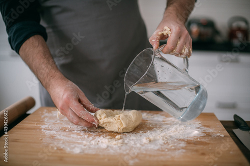 A male chef prepares noodle dough at home in the kitchen. Close up of hands with flour and dough