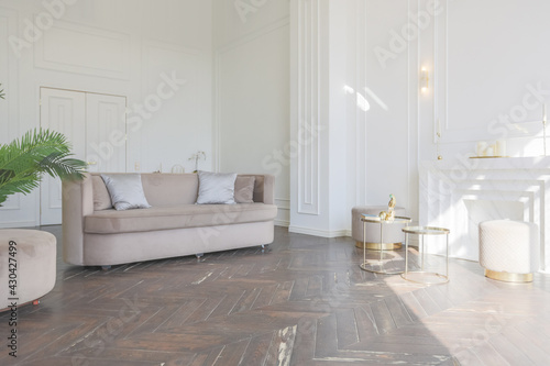 very light and bright interior of luxurious cozy living room with chic soft beige furniture with gold metallic elements  huge window to the floor and wooden parquet