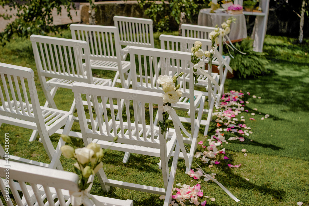Outdoor wedding ceremony, chairs decorated with flowers and ribbons stand in rows on the grass