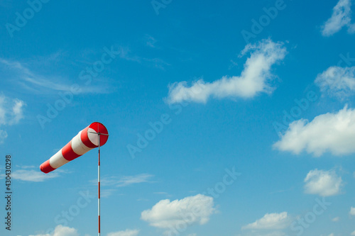 Windsock flag with red and white stripes on blue sky background. Wind speed meter