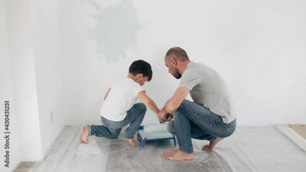 Caucasian man and boy paint the wall Father teaches son to paint with a roller Father and son make repairs together A friendly family Caucasian man and boy paint the wall Father teaches son to paint with a roller Father and son make repairs together A friendly family