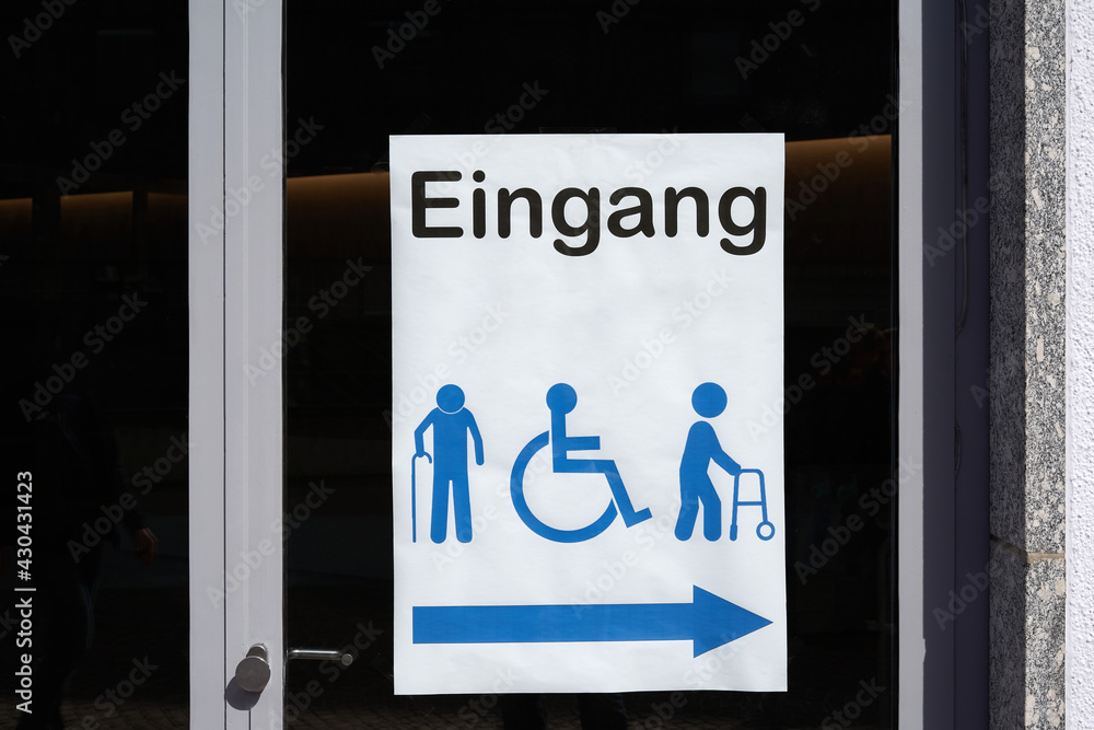 Sign on glass door saying: Entrance (germany: Eingang ). White paper with vector symbols of impaired and physically disabled people. Closeup. Sign on glass door saying: Entrance (germany: Eingang ). White paper with vector symbols of impaired and physically disabled people. Closeup.