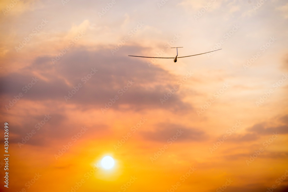 a glider sailplane soaring toward the evening setting sun with orange clouds a glider sailplane soaring toward the evening setting sun with orange clouds