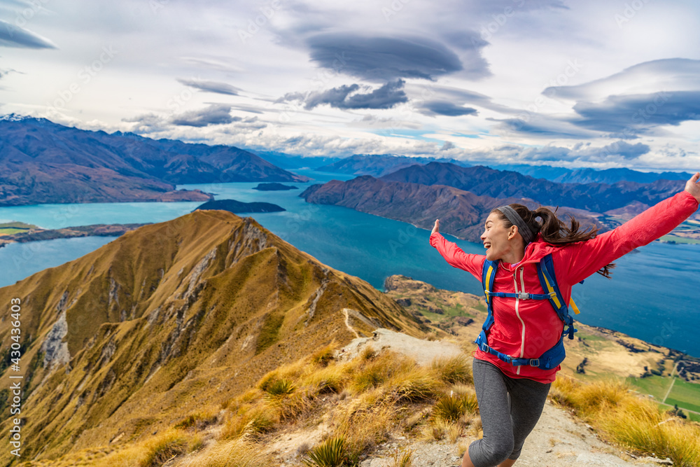 Travel post Covid-19 concept. Pent-up traveling demand concept. Hiker jumping of joy funny - woman hiking in New Zealand laughing having fun, joyful and aspirational at Roys Peak, South Island