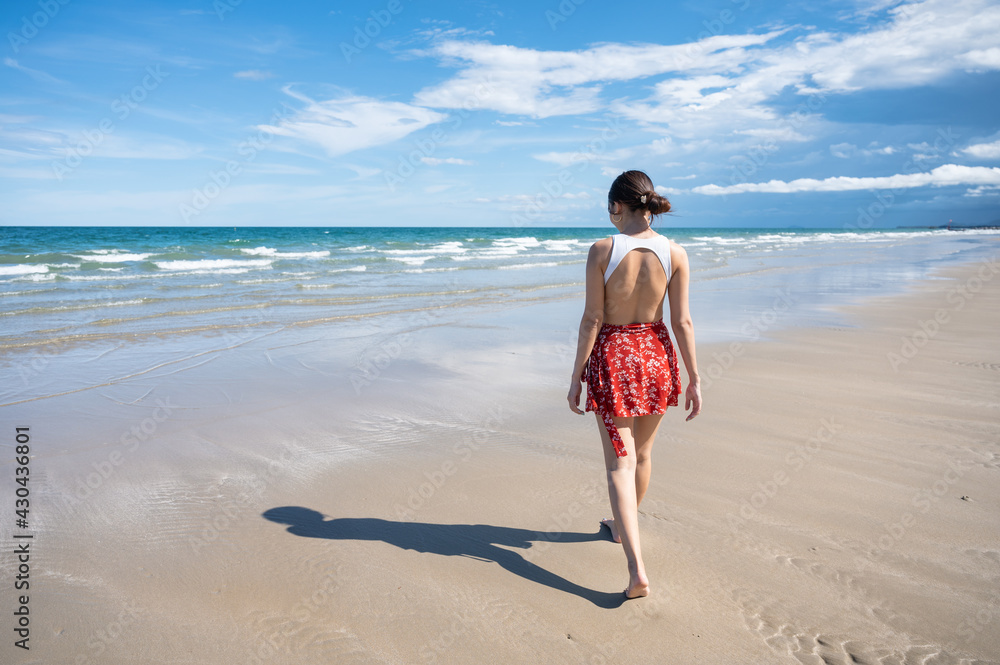 Attractive young asian woman in swimwear walking on the beach at tropical sea in sunny day