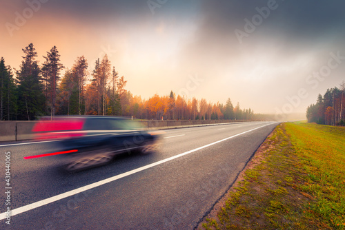Suburban autumn highway. Coniferous forest in the fog. The car goes on the road. Autumn morning. View from the side of the road. Russia, Europe. Beautiful nature.